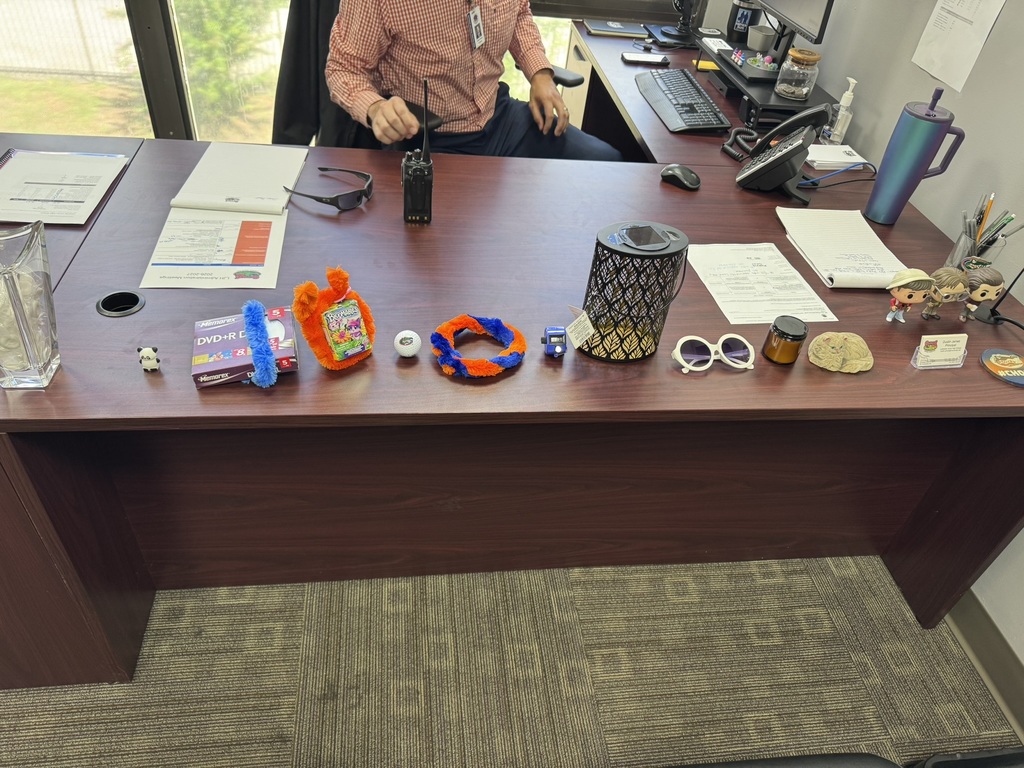 A desk with various items like a bracelet, glasses, pen, and bottle. A person sits in a chair.