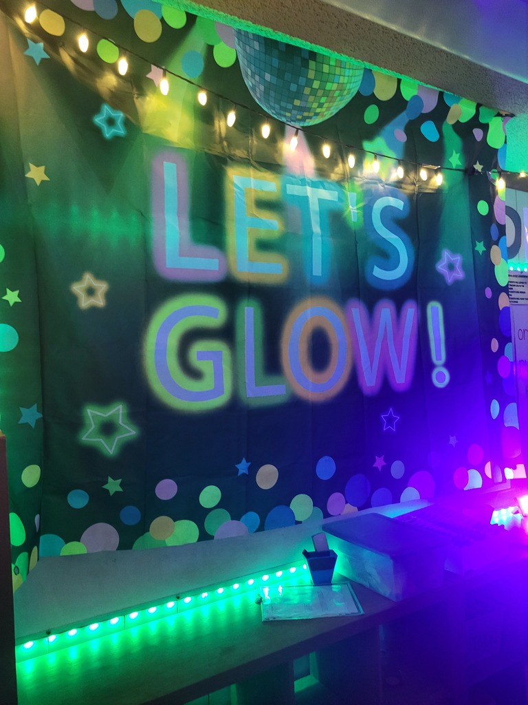 A colorful, glowing wall displays "Let's Glow!" with lights and polka dots. A disco ball hangs above with strings of lights.