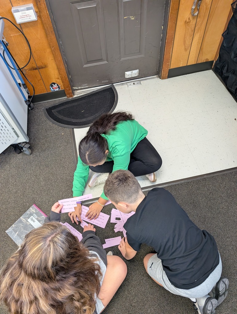 Three individuals work on a puzzle on the floor in a room with a gray door and a black mat.