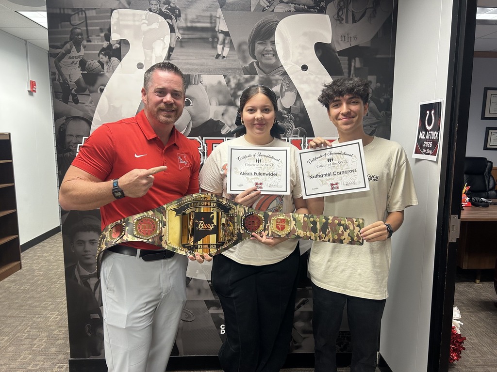 Three people in a room pose for a photo. Two hold certificates, one has a belt. A mural is behind them.