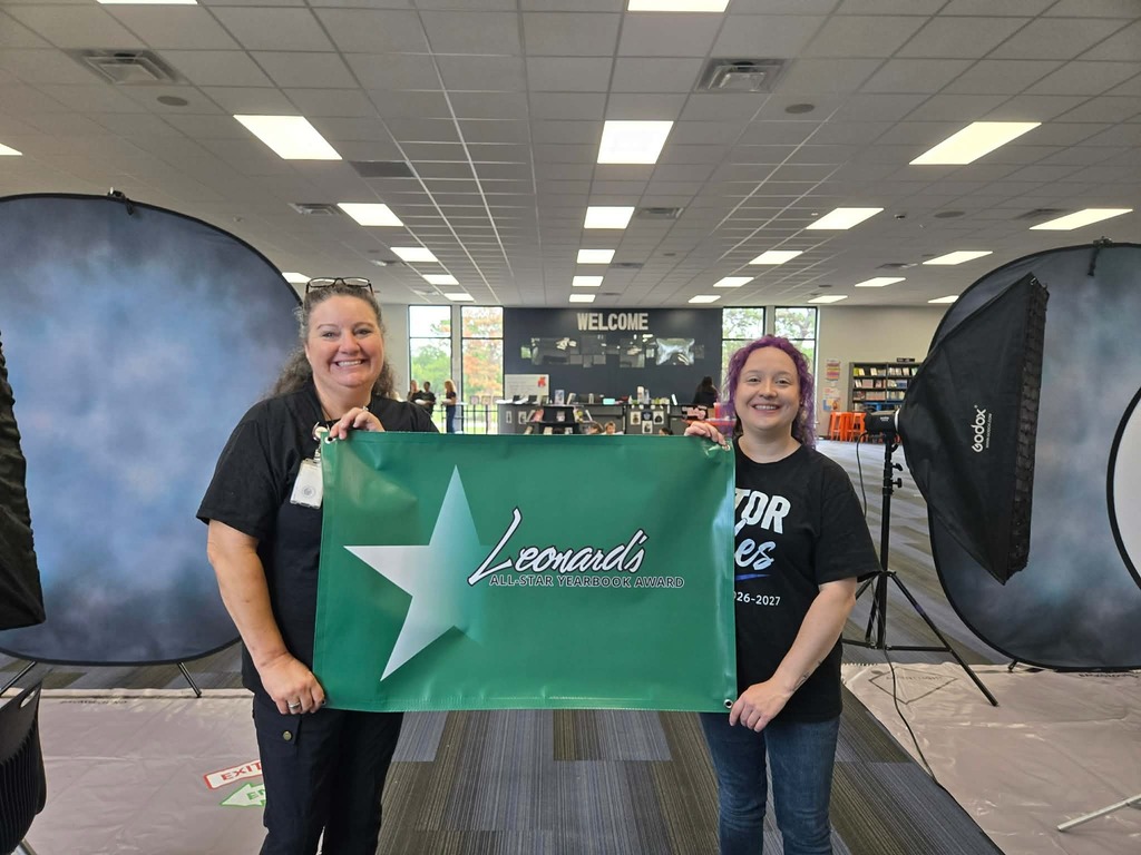 Two individuals hold a green banner with a star and text, standing in a studio with photography equipment.