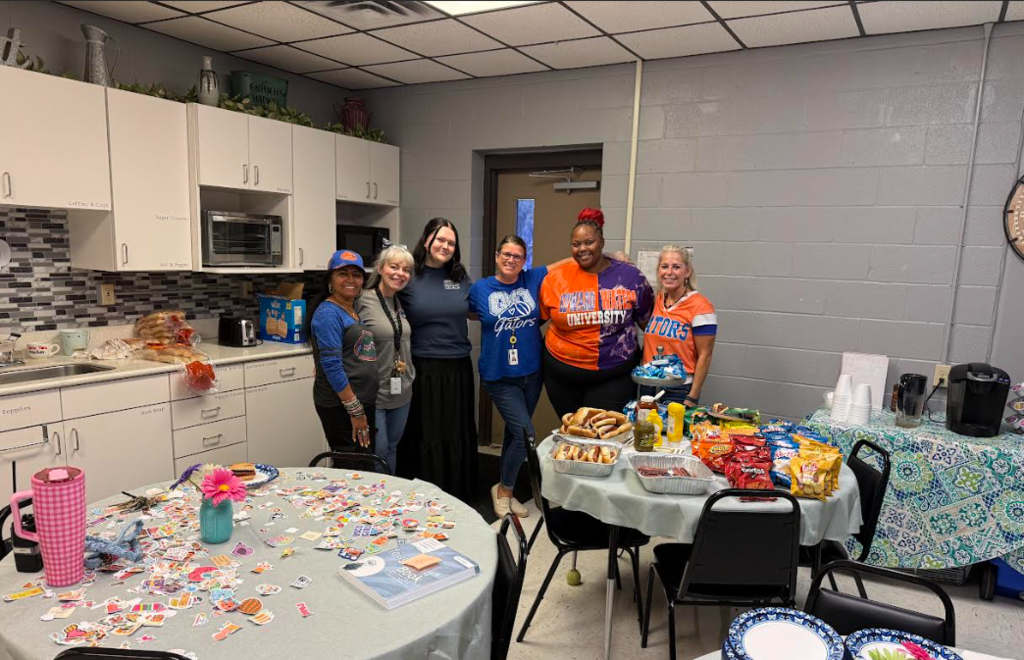 A group of six people standing together around tables with food and confetti in a kitchen.