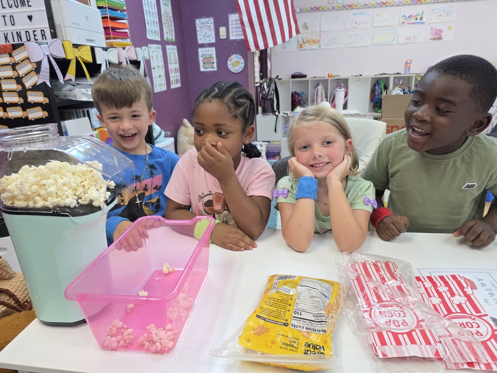 Children sitting at a table with popcorn, a popcorn machine, and boxes of snacks.