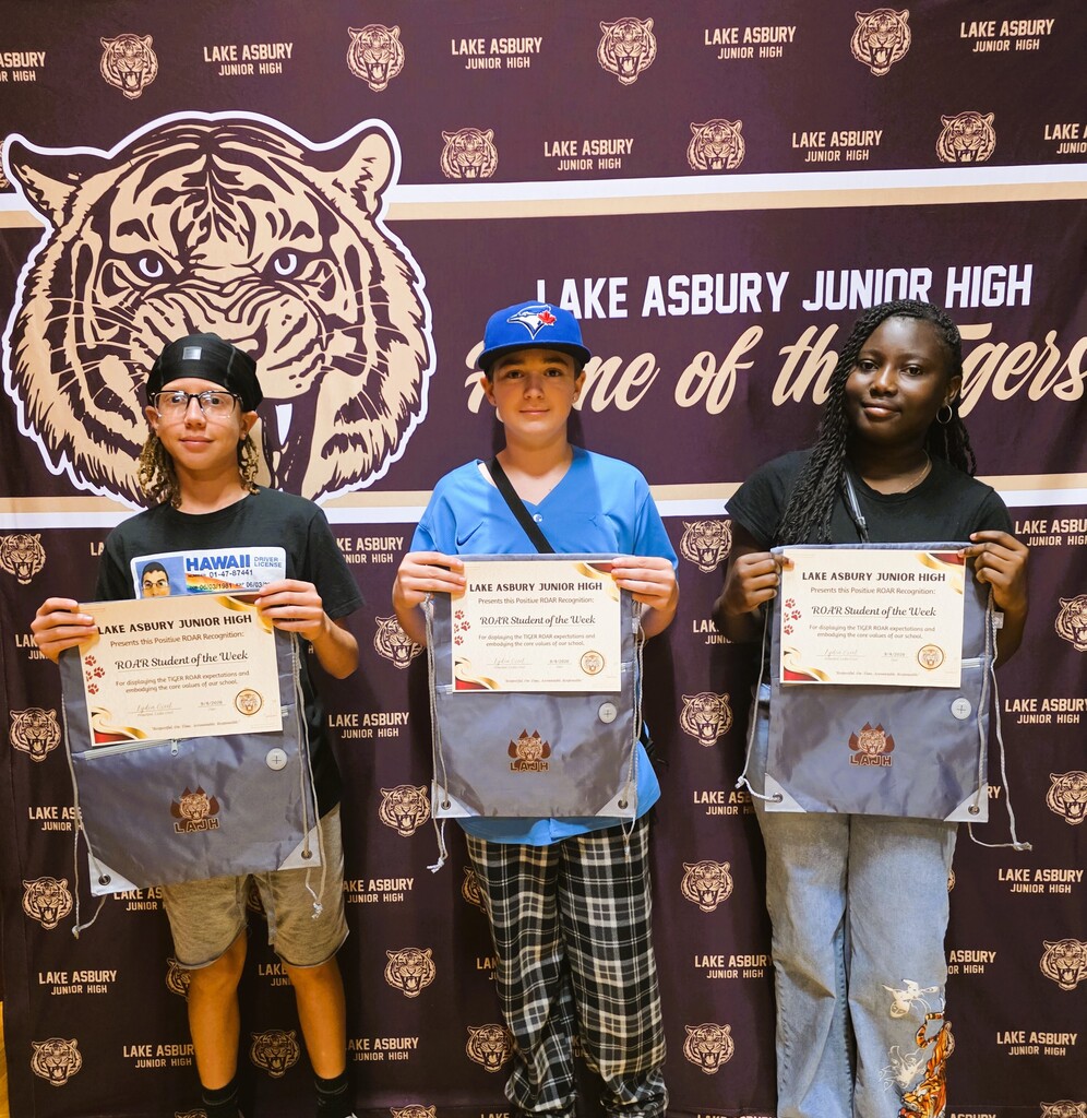 Four young people stand before a school banner. Each holds a certificate. A tiger logo is behind them.
