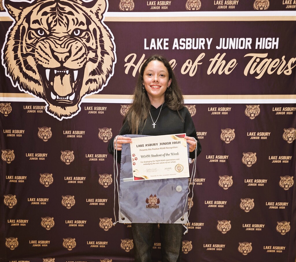 A young woman poses with a certificate in front of a wall with a tiger logo.