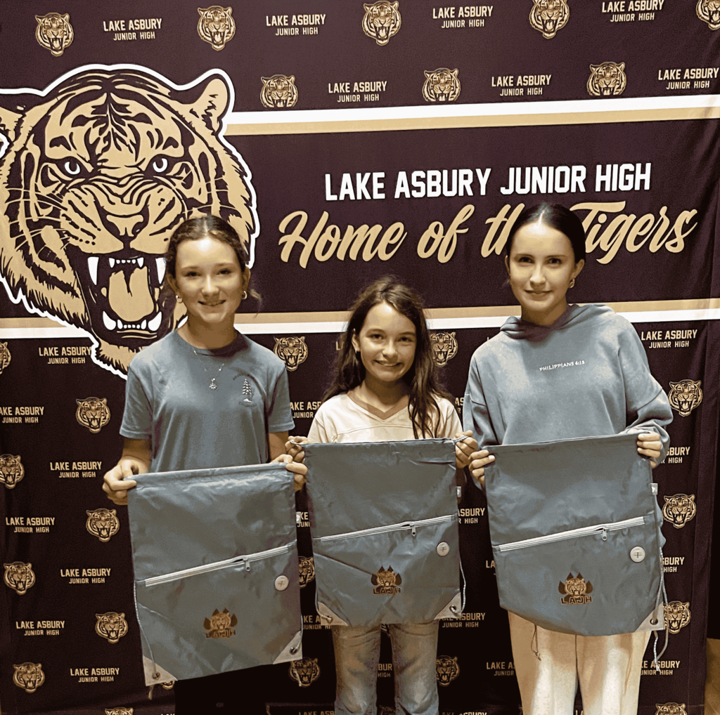 Three children pose for a photo holding bags in front of a banner with a tiger.