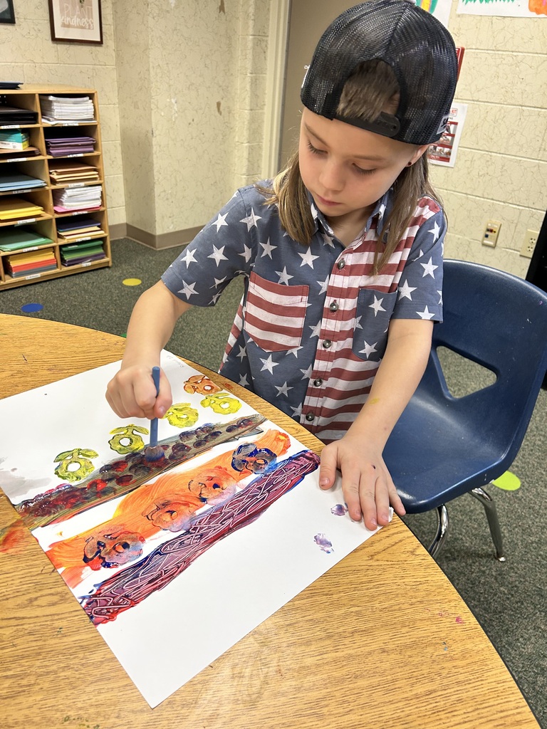 A young person painting a large canvas with multiple colors. The table is wooden.