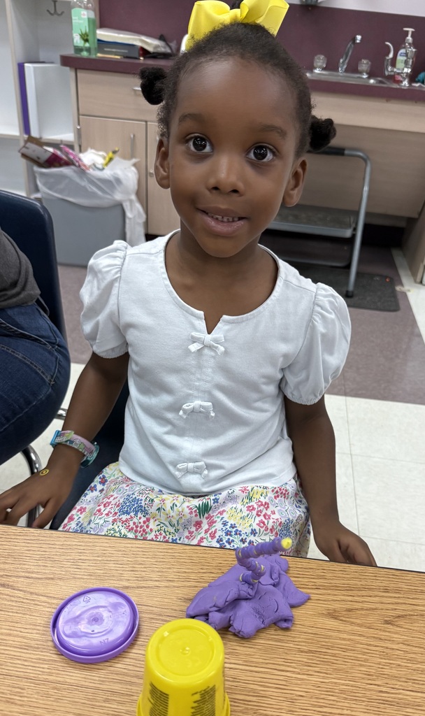 A young girl sitting at a table creating with dough and beads.