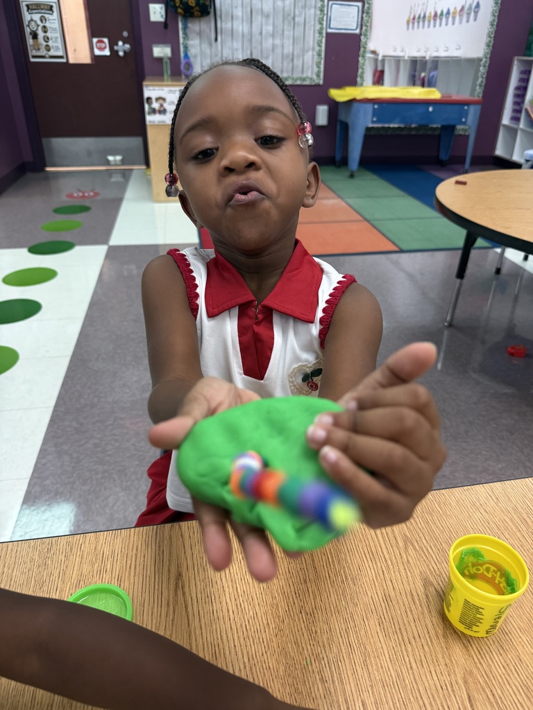 A young girl sitting at a table creating with play-doh and beads.