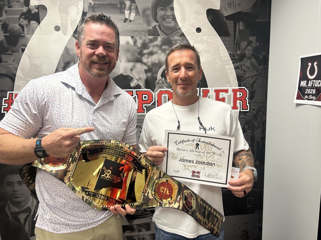 Two men pose for a photo with a belt and certificate. They stand in front of a collage of sports-related images.