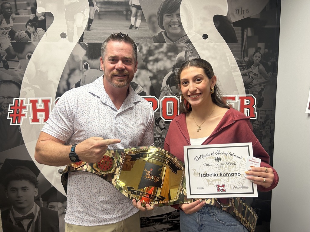 A man and a woman stand in front of a wall with sports images and text. The man holds a gold belt, and the woman holds a certificate.