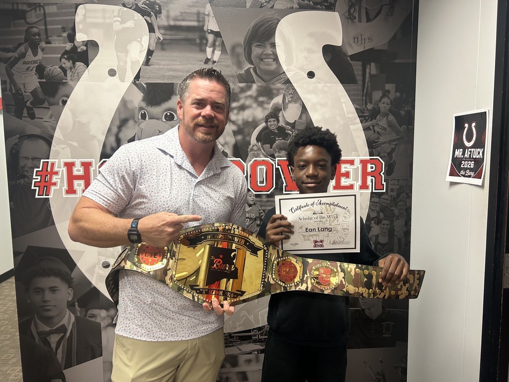 Man and child in front of wall with sports photos. Man holds belt, child holds certificate.