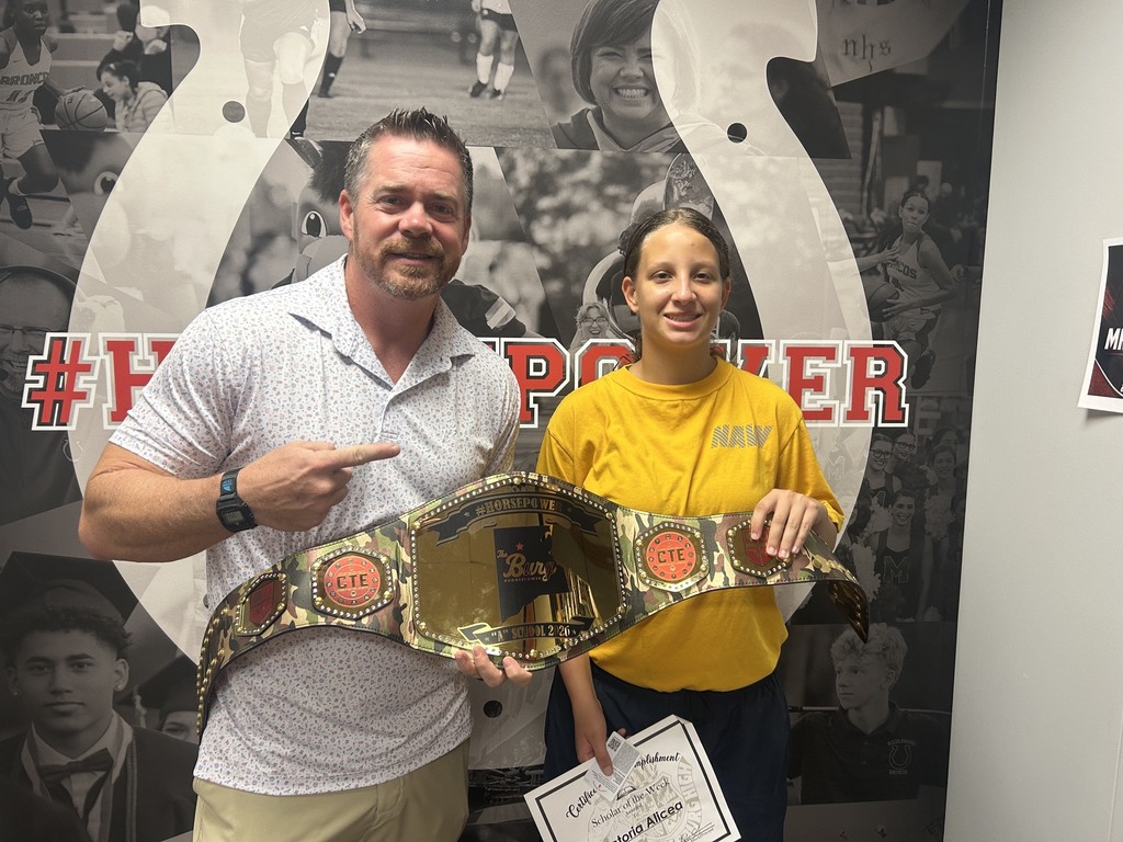 Man and woman posing with a championship belt in front of a wall with a horseshoe.