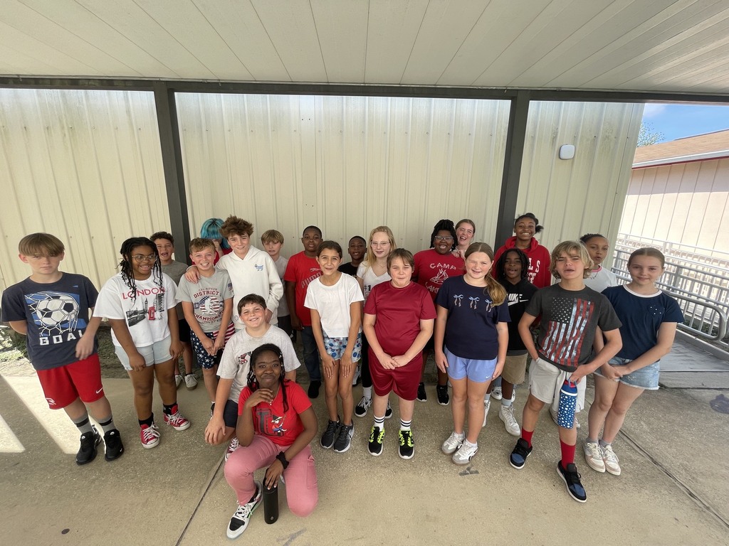 A group of children poses for a picture in a covered outdoor area. Some wear athletic attire.