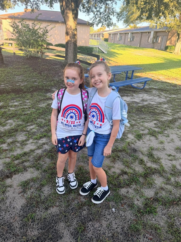 Two young girls stand close together in a schoolyard with a tree.