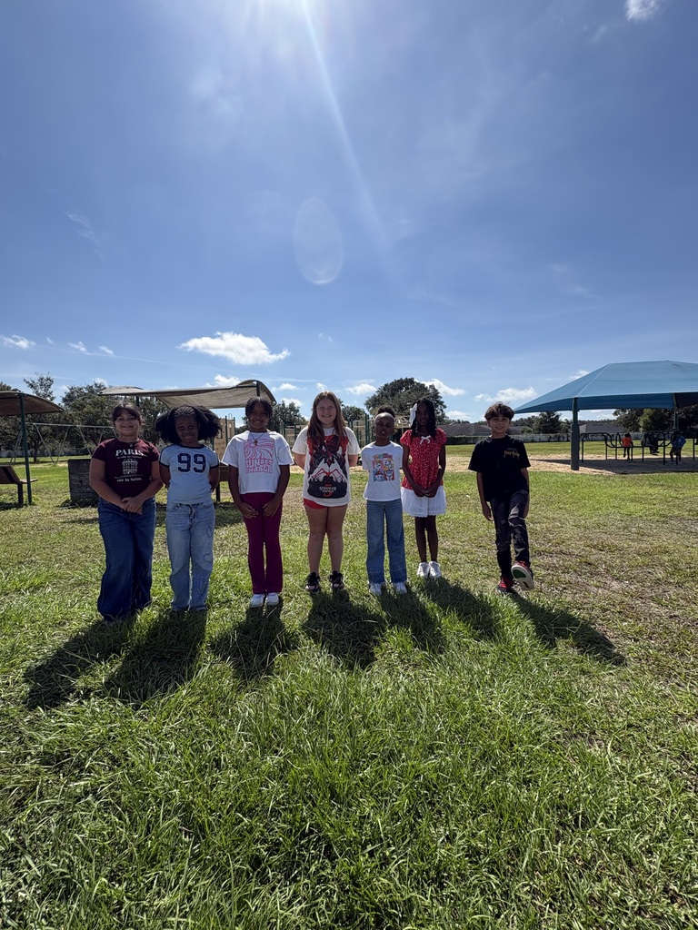 Several children wearing red white and blue stand in a line on a grassy field