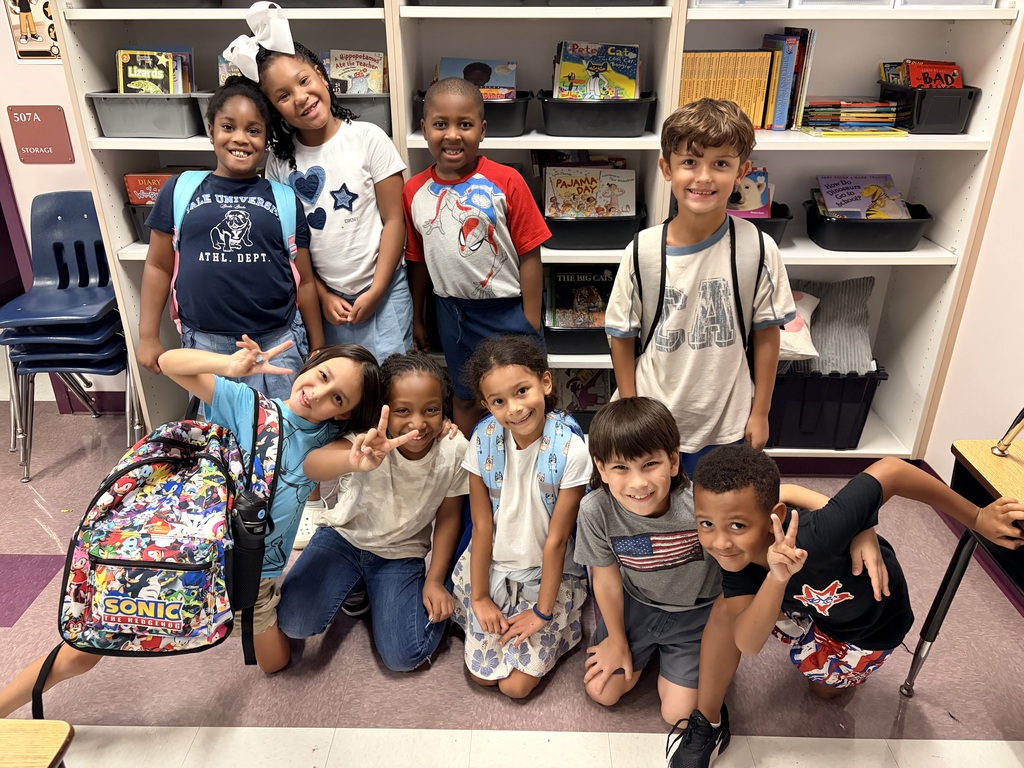 Group of children wearing red, white, and blue in a classroom, smiling and posing.