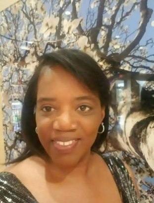 A woman with short hair smiles at the camera in front of a floral and abstract tree mural.