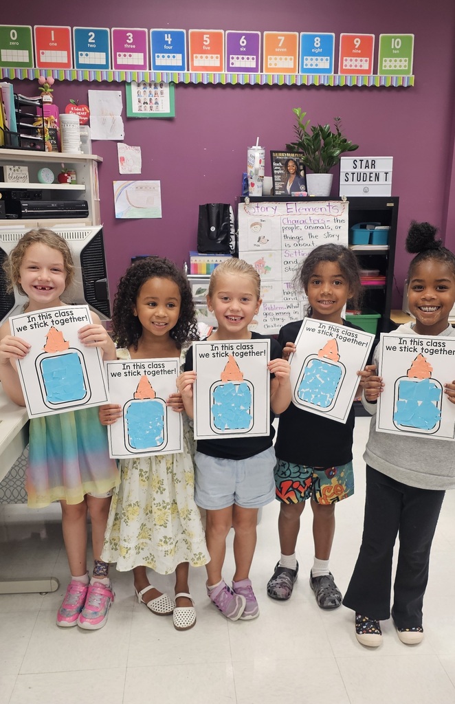 Five children in a classroom hold their cut/glue projects. They are smiling and standing together. 