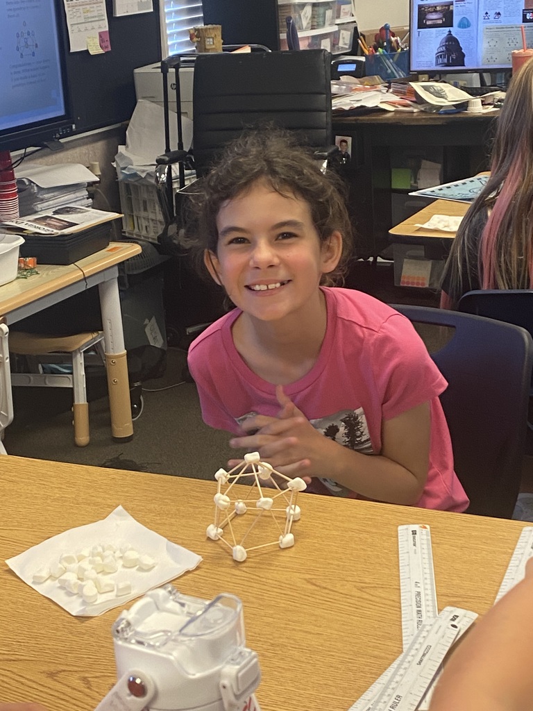 A girl smiles in a classroom, seated at a desk with a model in front of her.