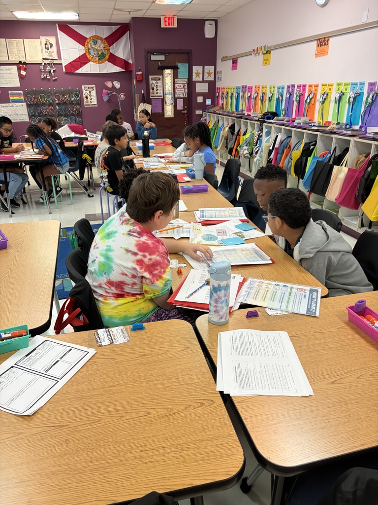 A classroom with children seated around desks, working on activities with papers and items on the table.