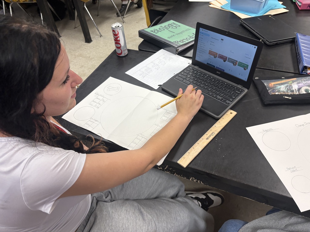 A woman in a white shirt and gray pants works on a laptop at a table.