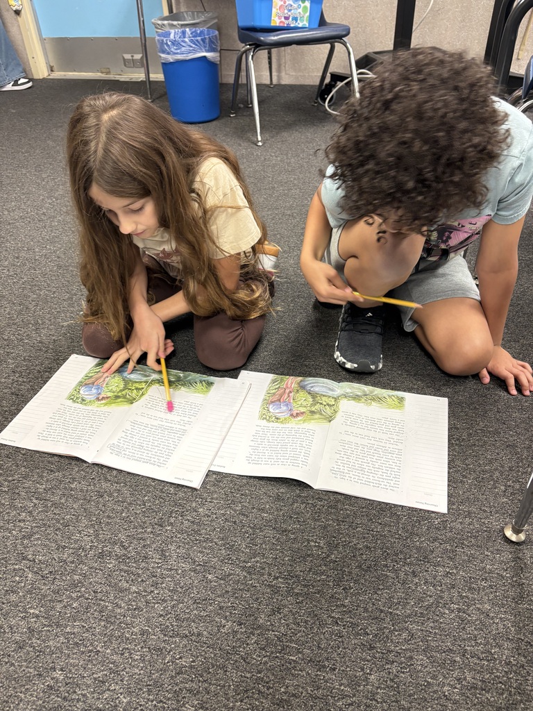 Two children, one with brown hair and one with curly hair, are kneeling on the floor and looking at a book.