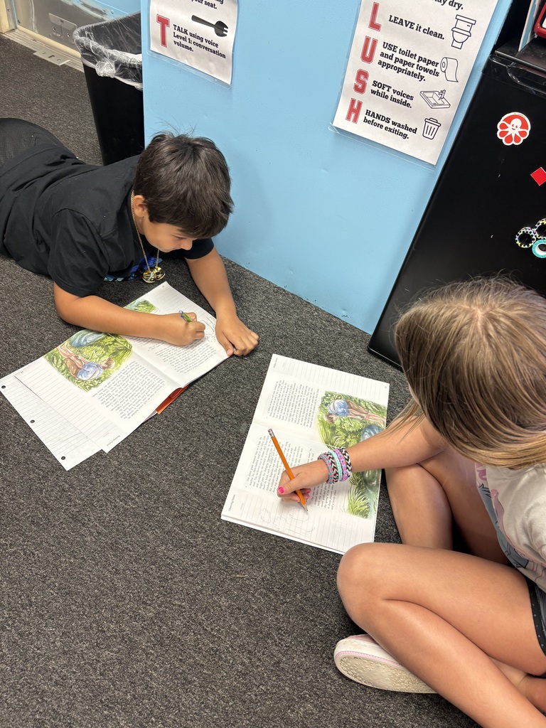 Two children, one reading and one writing, sit on the floor with open books and pencils.