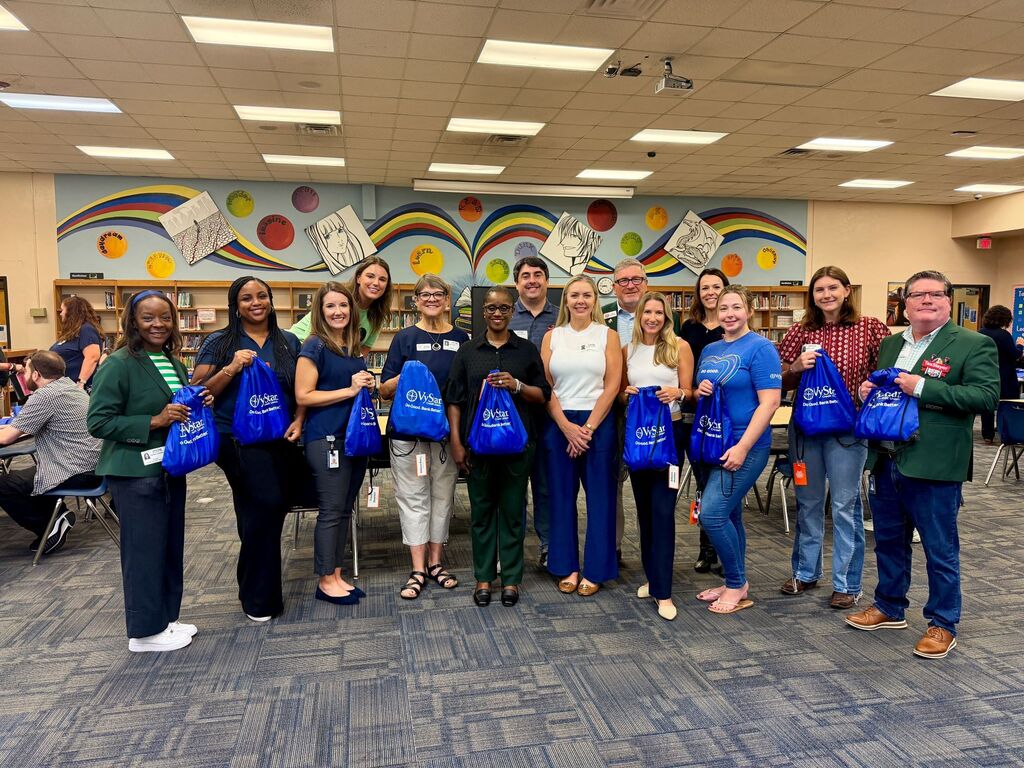 Group of people in a room holding blue bags, standing in front of a colorful mural.
