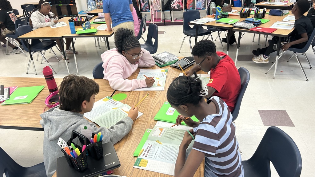 Four children work together at a desk in a classroom. 
