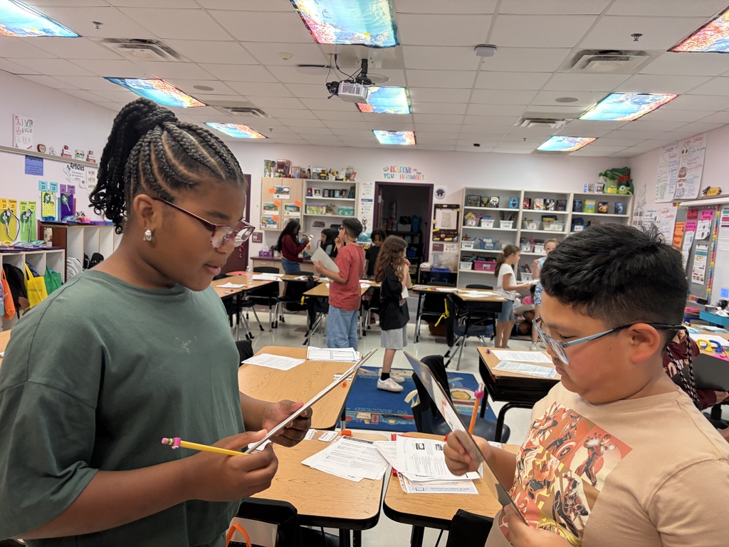 Two students, one with glasses, are standing at a desk reviewing papers 