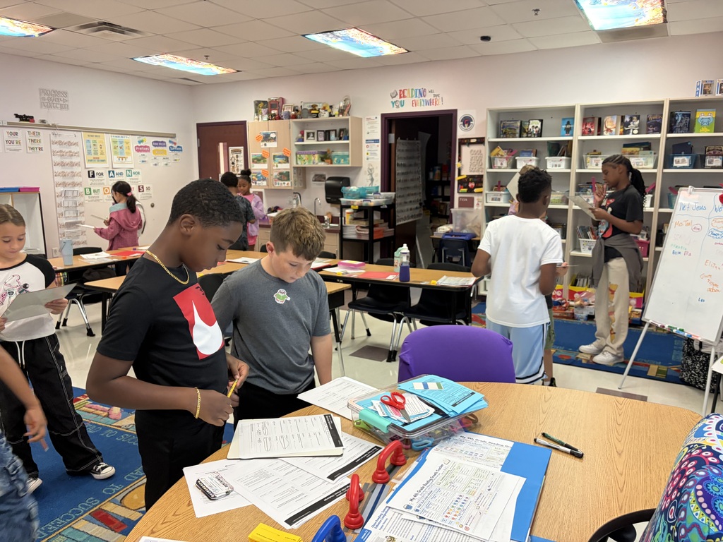 In a classroom, students are gathered around tables. 