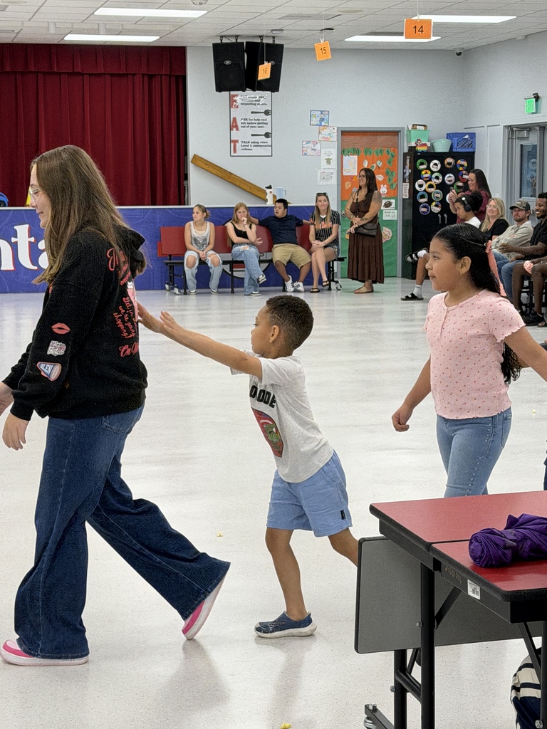 A woman and two children dance in a hall. The woman wears a black hoodie and blue jeans.