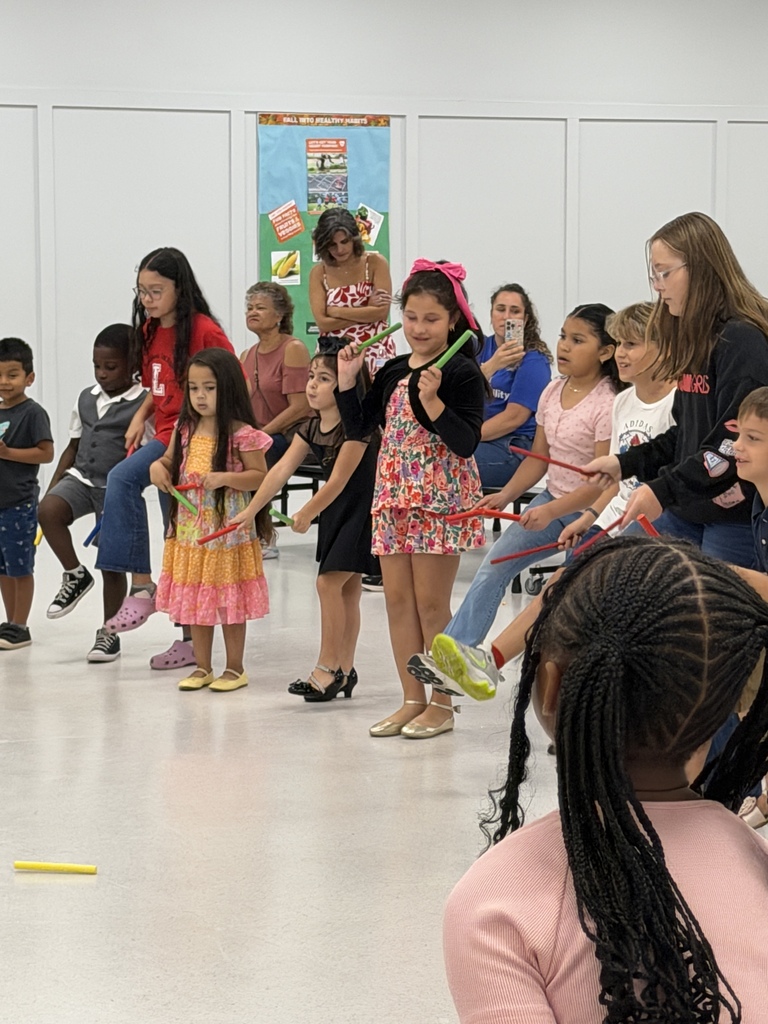 A group of children and adults stand in a room, holding and playing with musical instruments.