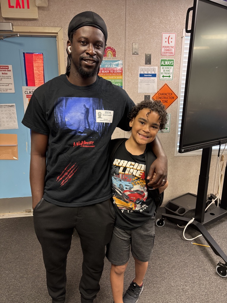 Man and child stand close in a room, both wearing black T-shirts. They are near a blue door.
