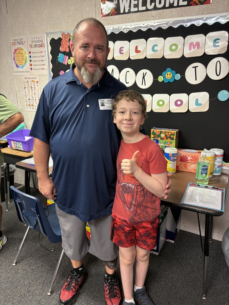Man and boy standing next to each other in front of a classroom with a welcome sign.