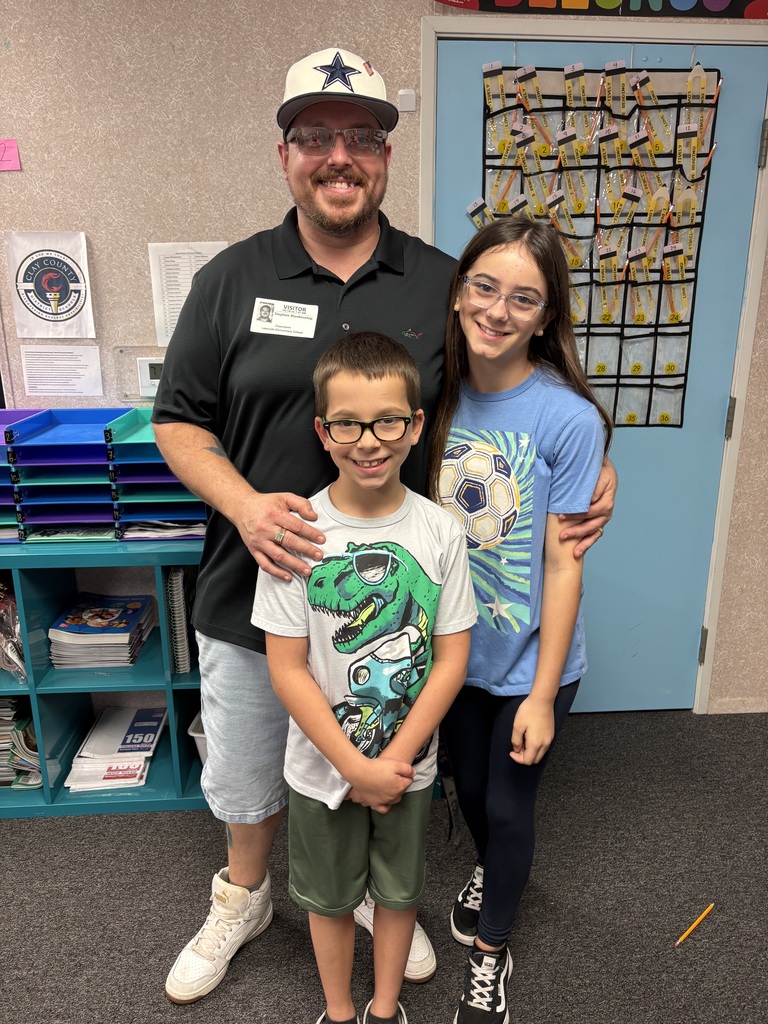 A man and two children stand close together, smiling. The man wears glasses and a hat.