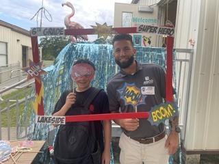 A man and a child stand in a photo frame with a backdrop of pink flamingos.