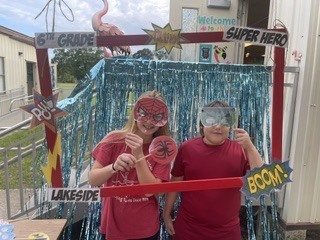 Two children wearing masks stand before a photo booth. One holds a lollipop, the other wears goggles.