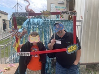 A man and child wearing superhero masks stand behind a photo frame with "Super Hero" and "Boom" text.