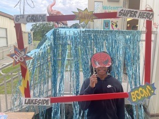 Person in superhero mask stands in front of blue curtain with "6th Grade" and "Lakeside" text.