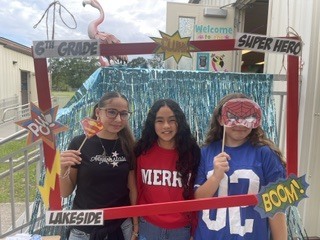 Three young girls in front of a photo booth. Each holds a mask: one pink, one blue, and one red.