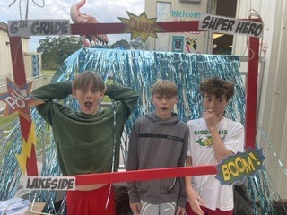 Three boys pose for a photo at a Lakeside event, standing behind a photo frame with "6th Grade Super Hero" on it.