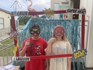 Two children wearing superhero masks, one with a red cape, pose in front of a photo frame.