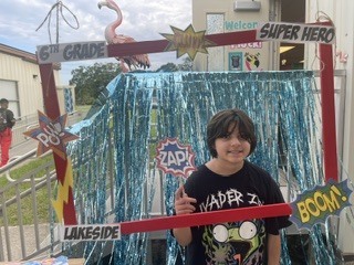 A young boy in a black t-shirt stands by a photo booth adorned with blue streamers and signs.