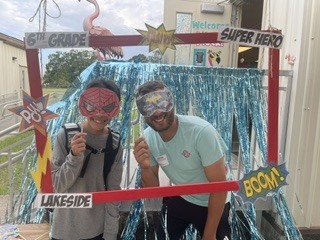 Two individuals wearing masks and goggles stand next to each other in front of a colorful backdrop.
