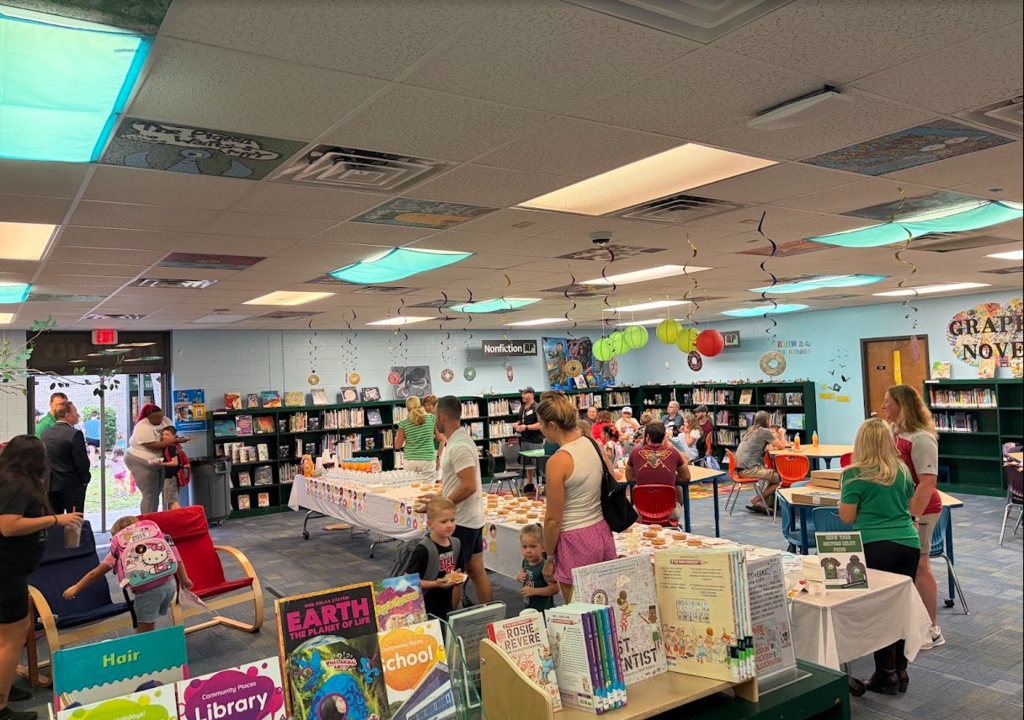 A library space with tables covered in books. People in different clothing walk around and browse.