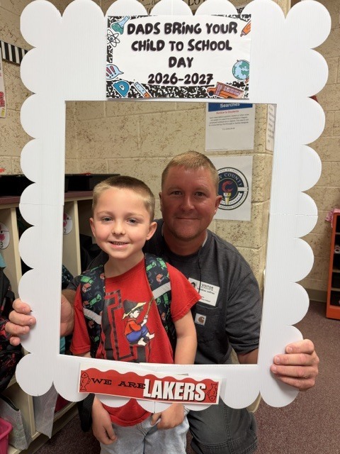 Man and child in a white frame with "Dads Bring Your Child to School Day" and "We Are Lakers" text.