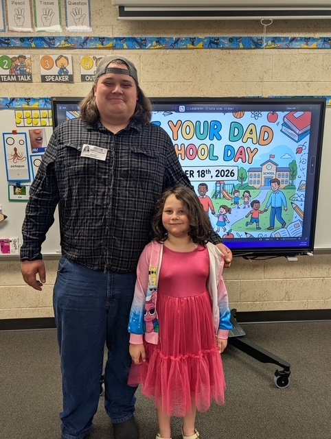 A man and a young girl stand in front of a screen displaying "Your Dad School Day."