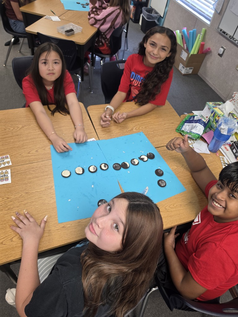 Four students sitting at a table, engaged in an activity with buttons on a blue board.